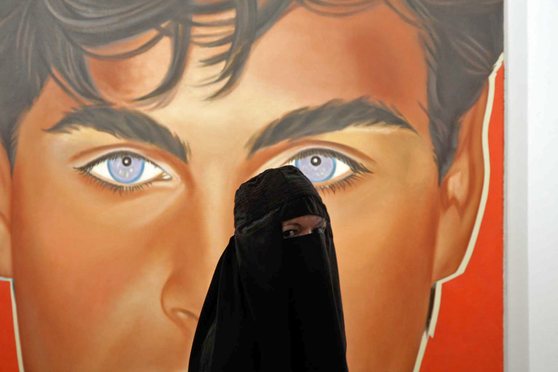 A woman wearing a burka at the art fair, in reality a performance role by Preeti Chandrakant, here in front of a painting at the opening of Art 41, 2010