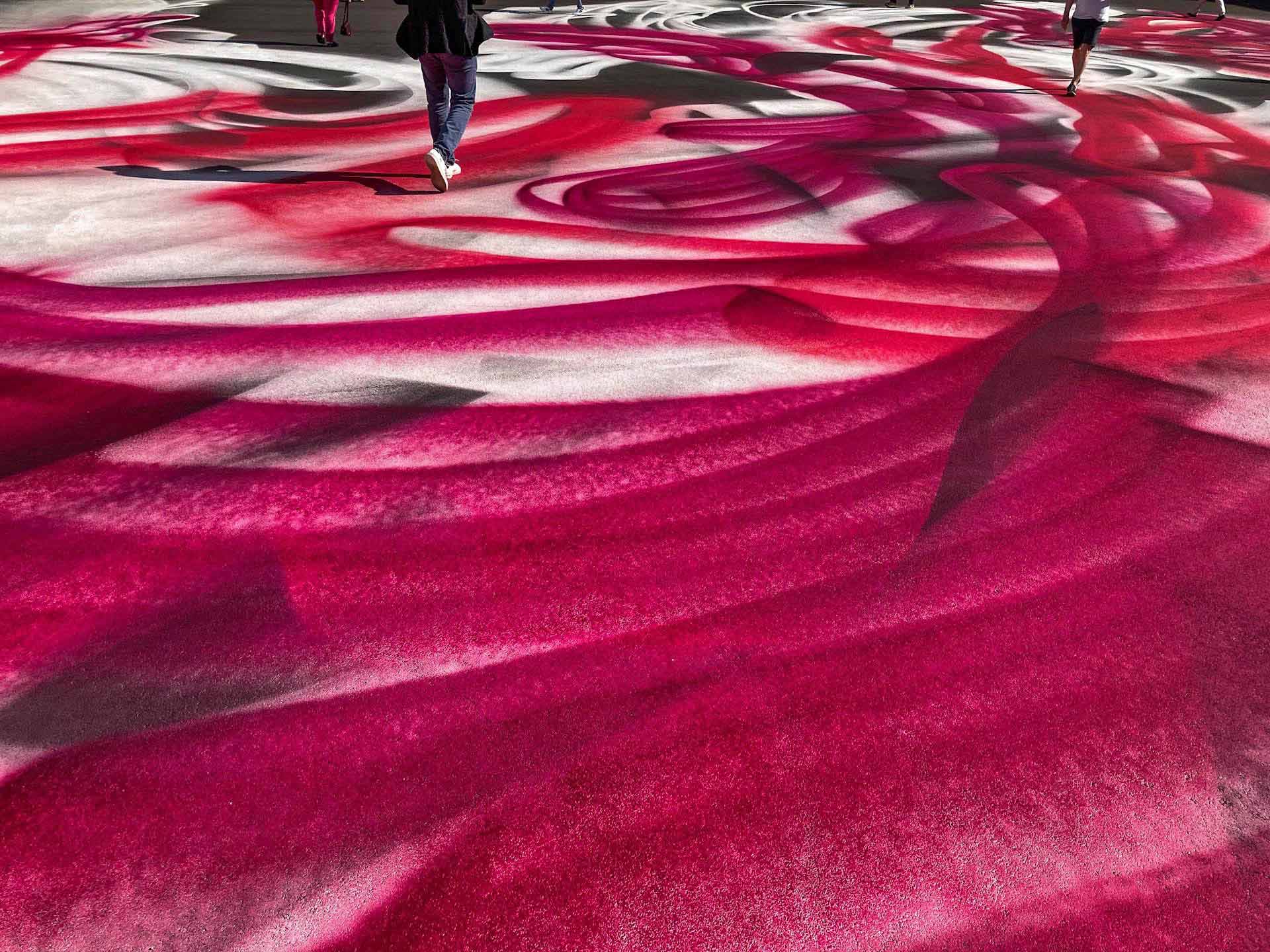 Walking on the painting – Grosse hat den Messevorplatz in Basel in ein Kunstwerk verwandelt: Mit einer Spritzpistole sprayte sie ausladende Graffiti in Magenta Rot auf den Platz selbst und die Gebäudeflächen.